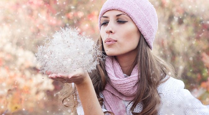 woman wearing pink scarf and hat blowing weeds in the air