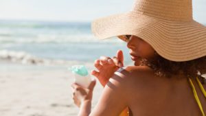 woman wearing sunhat on beach applying sunscreen 