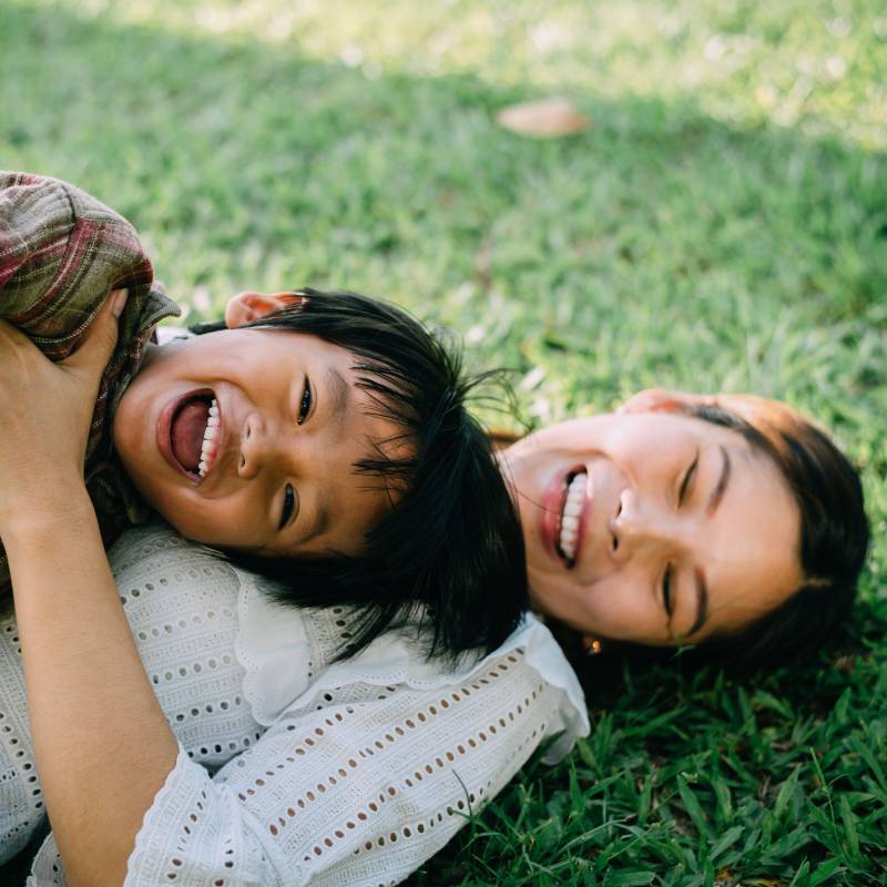 Mother and son laughing while laying on the grass