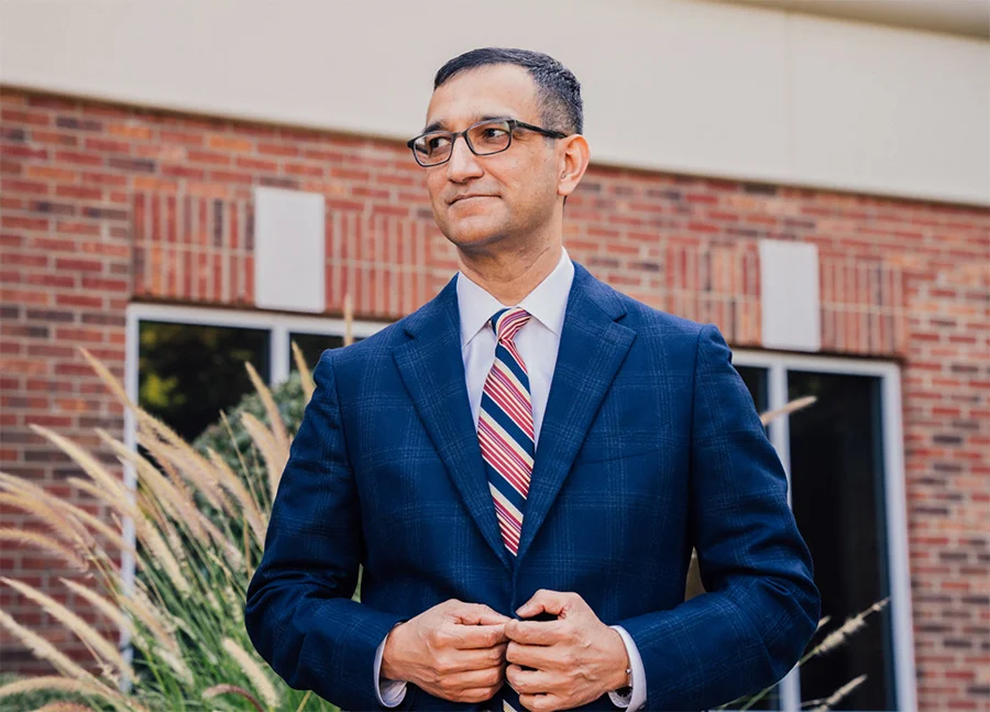 Dr. Haque in a blue suit and glasses standing outside in front of a brick building.