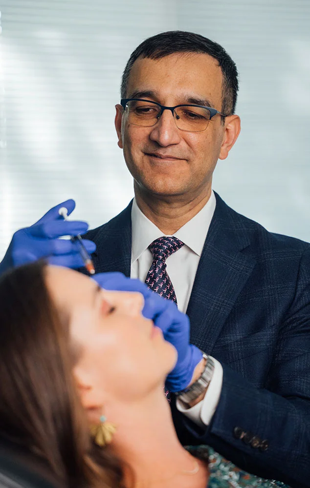 Dr. Haque, dressed in a professional suit, carefully administers a facial cosmetic injection to a patient during a clinical treatment session. - Botox Wrinkle Relaxers in Charlotte, NC