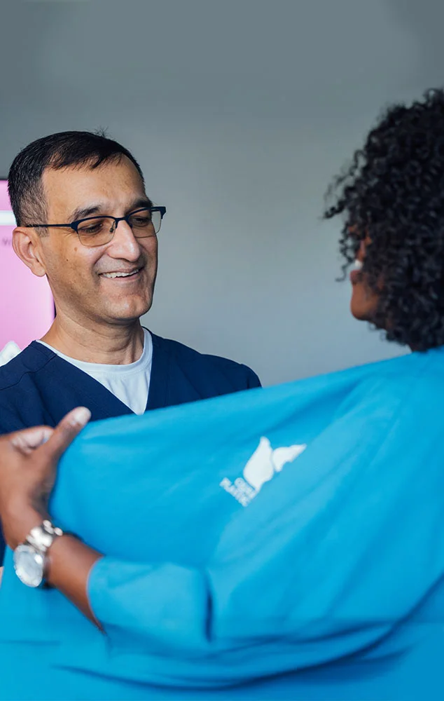 Dr. Haque smiling while talking with a patient in a blue medical gown. - Breast Cancer Reconstruction in Charlotte, NC