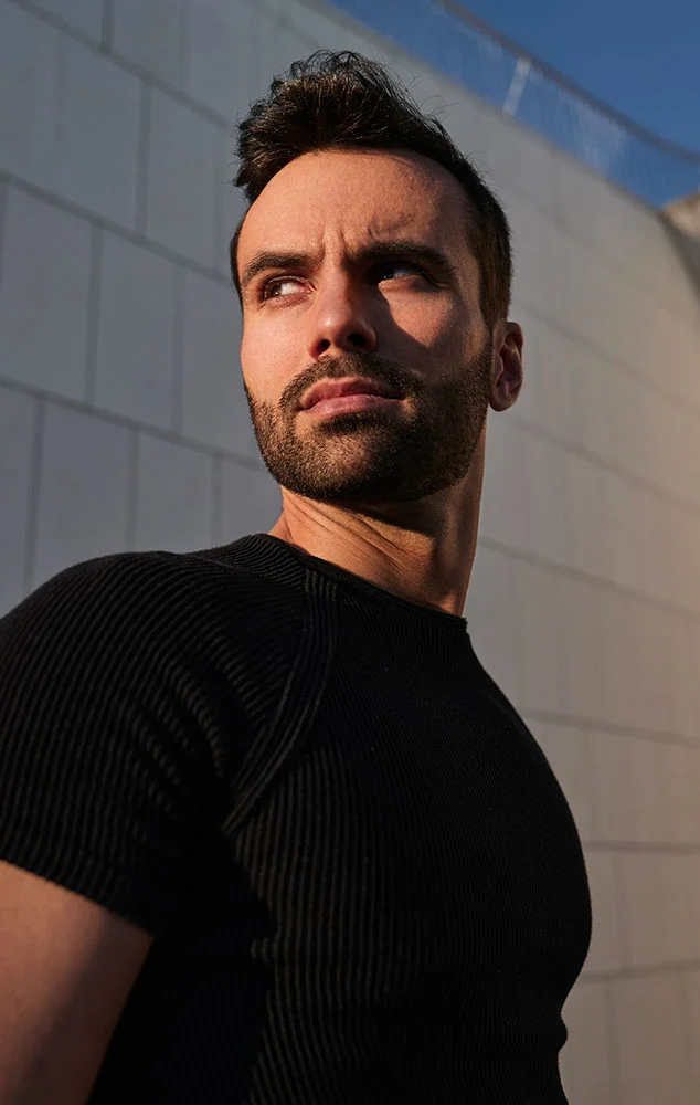 A man in a black shirt looking off-camera against a white tiled wall. - Gynecomastia in Charlotte, NC