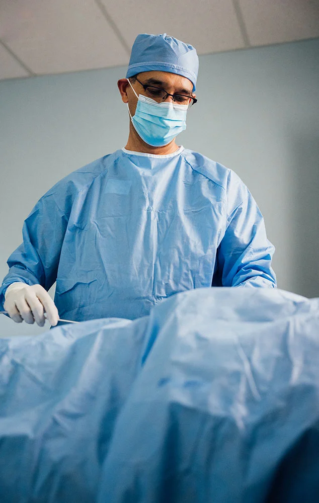 Dr. Haque in blue surgical scrubs, mask, and cap, performing a medical procedure. - Male Liposuction Bodytite in Charlotte, NC
