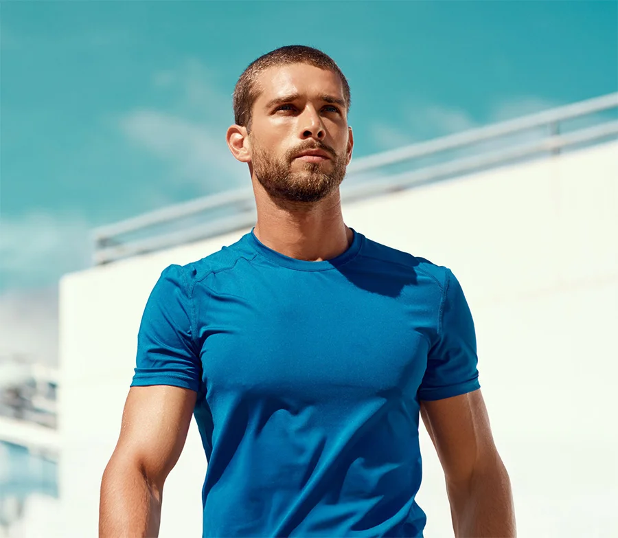 An athletic man in a blue shirt looking forward against a bright outdoor background.