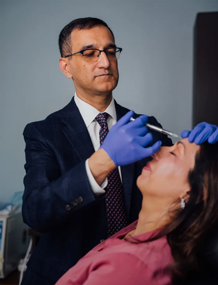 Dr. Haque wearing blue gloves while performing an injection on a patient's forehead.
