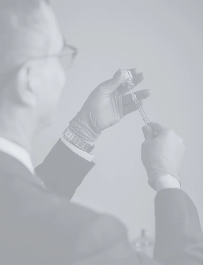 Faded image of Dr. Haque's hands in blue gloves preparing a syringe from a vial.