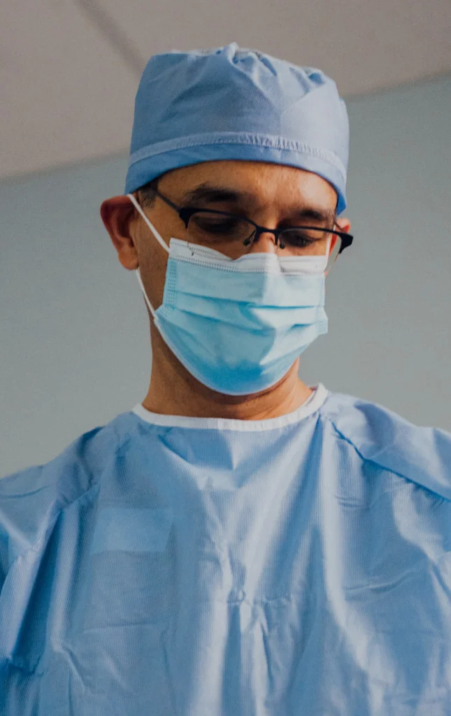 Dr. Haque in blue surgical scrubs and a mask performing a procedure with a medical tool.
