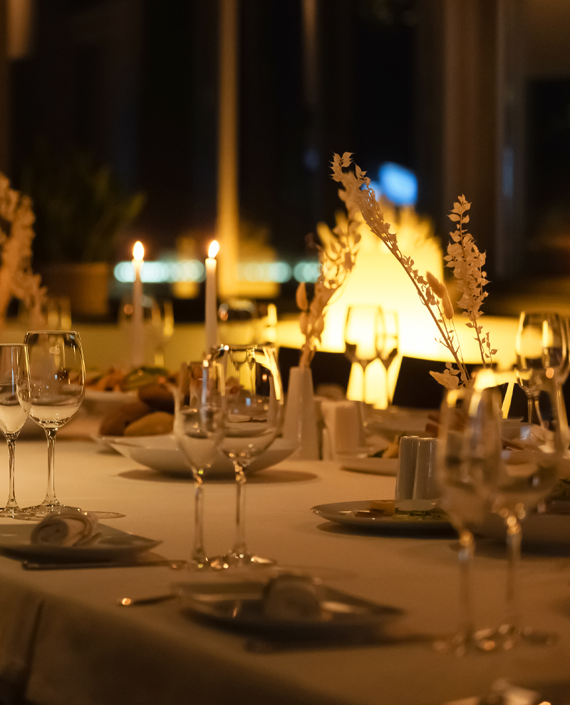Long dinner table set with wine glasses and candles in a warm, dimly lit room.