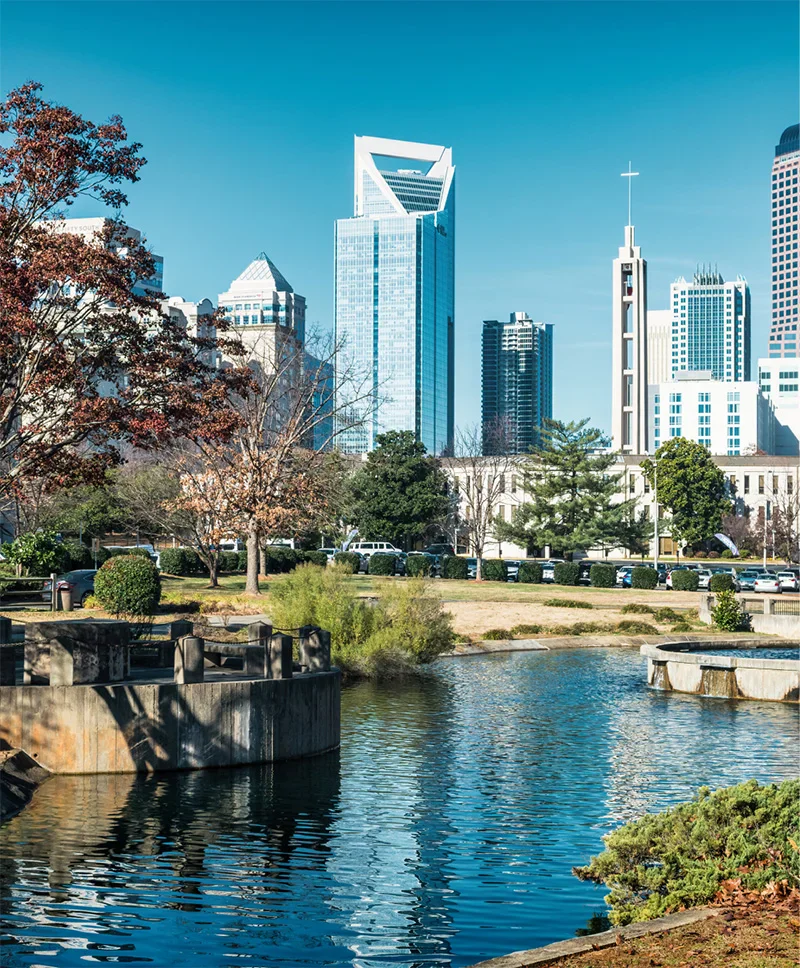 A scenic view of the Charlotte skyline and a modern skyscraper reflected in a park pond.