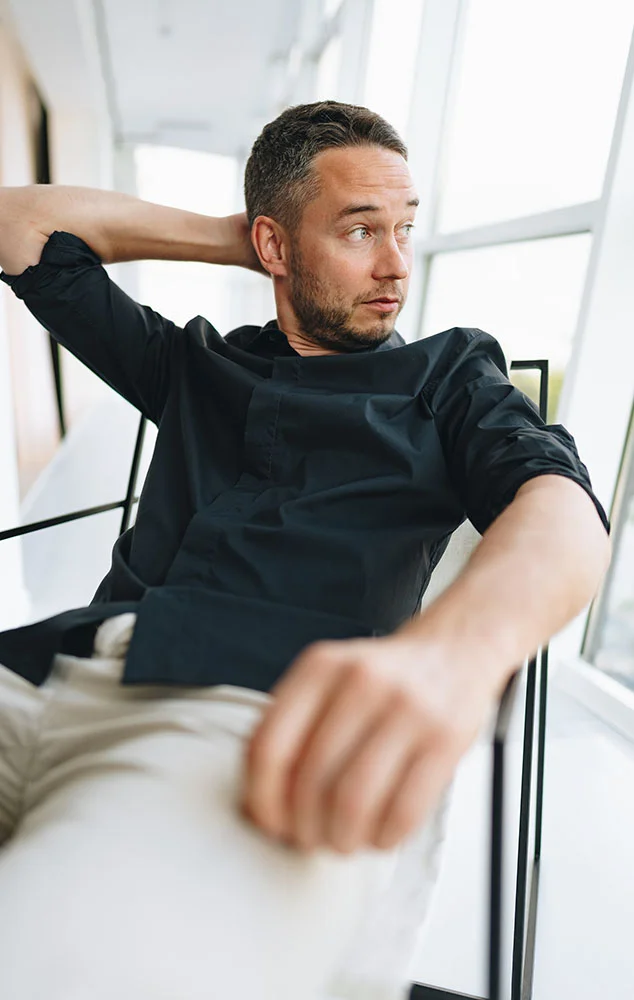 A man in a black shirt sitting and looking toward a window. - Trigger Finger in Charlotte, NC