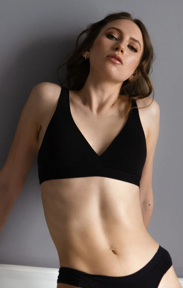 A woman in black athletic wear posing against a grey wall to show her toned midsection. - Tummy Tuck in Charlotte, NC