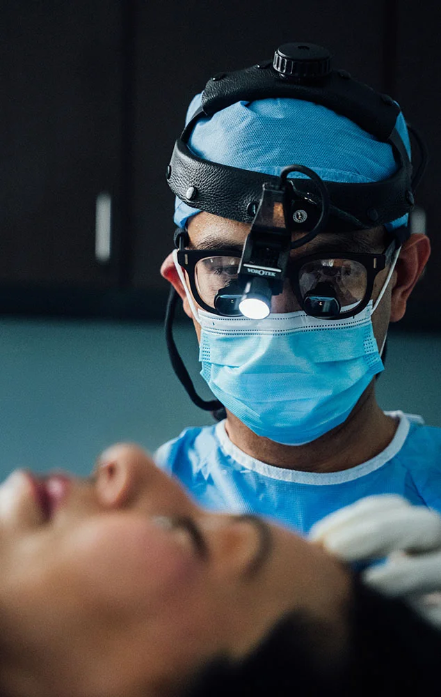 Dr. Haque wearing surgical loupes and a mask while treating a patient. - Upper Blepharoplasty in Charlotte, NC